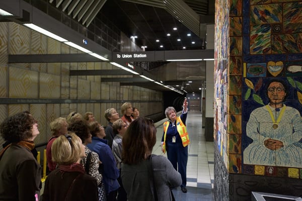 A Metro Art tour guide discusses the artwork at Universal City Station. The ceramic mural by Margaret Garcia, called Tree of Califas, marks the historic site of the Campo de Cahuenga, where in 1847 Mexico relinquished control of California to the United States.