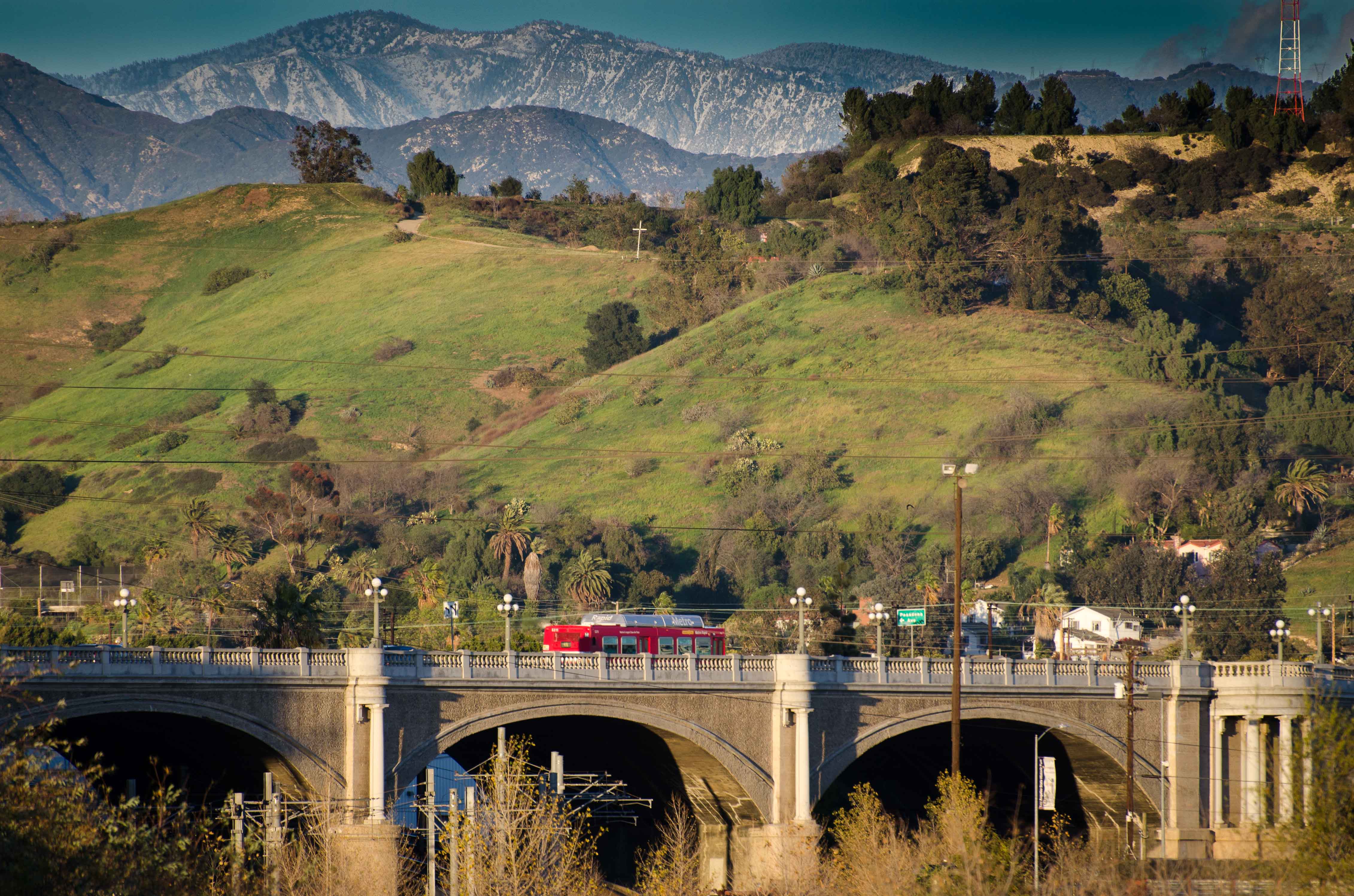 ART OF TRANSIT: A Metro Rapid bus crosses the Broadway bridge over the Los Angeles River on Wednesday afternoon, the day after a storm greened the local hills and dumped snow in the San Gabriel Mountains. Click above to see larger. Photo by Steve Hymon/Metro.