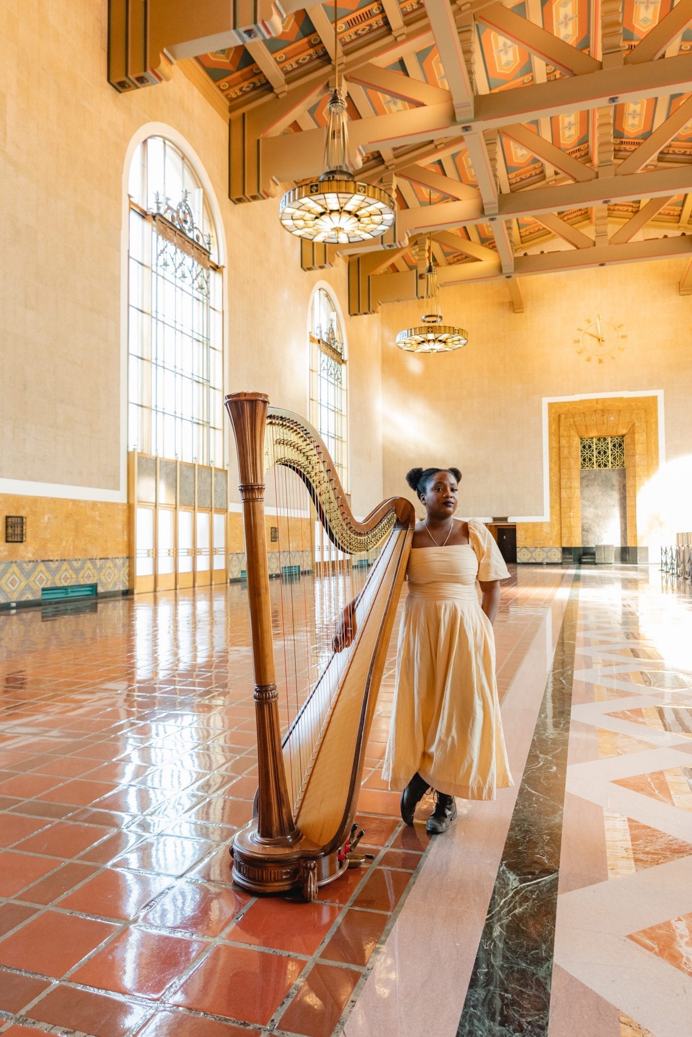 Woman stands in historic Union Station Ticketing Hall with a harp in mid-morning sun
