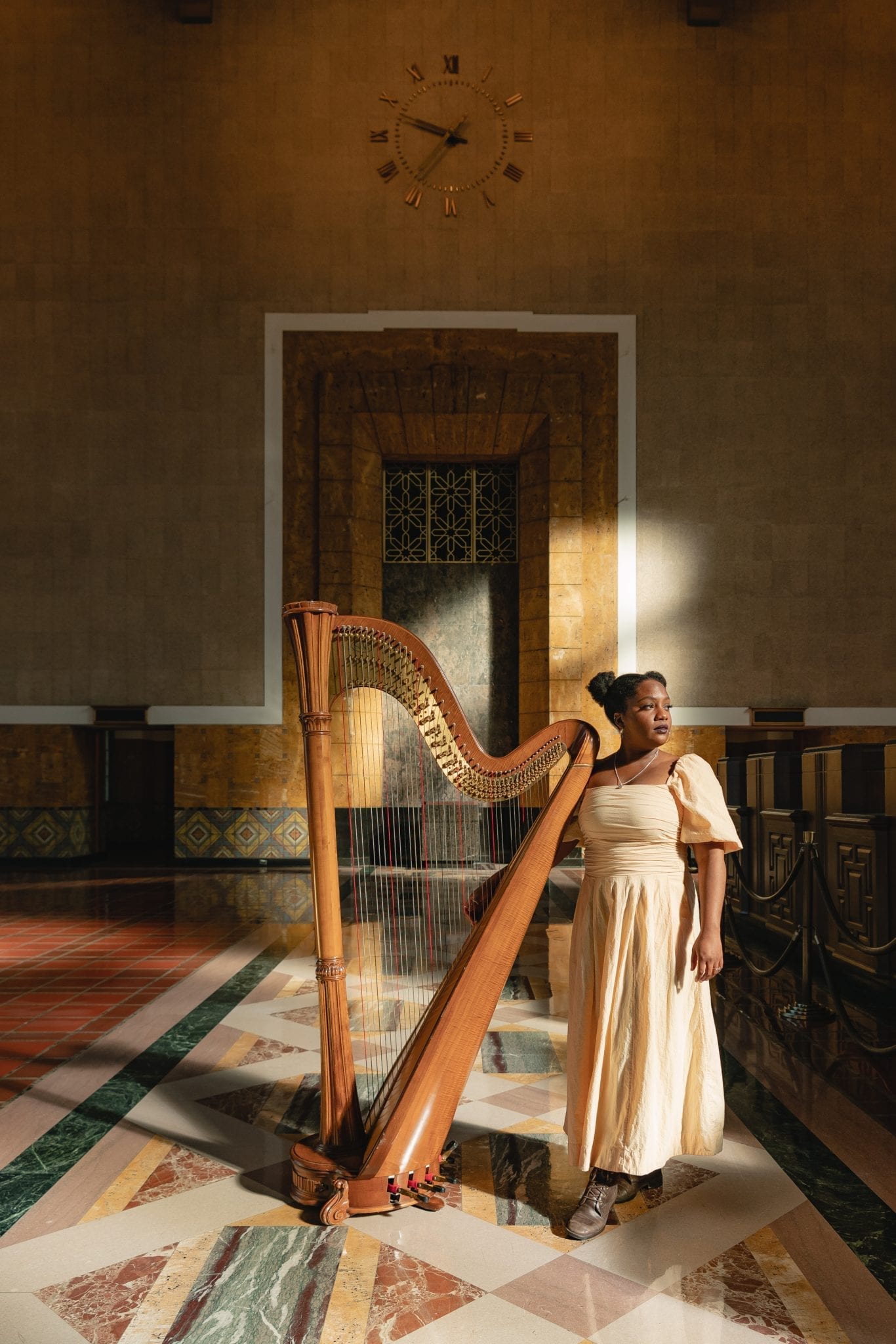 Woman stands in historic Union Station Ticketing Hall with a harp and light dancing behind her