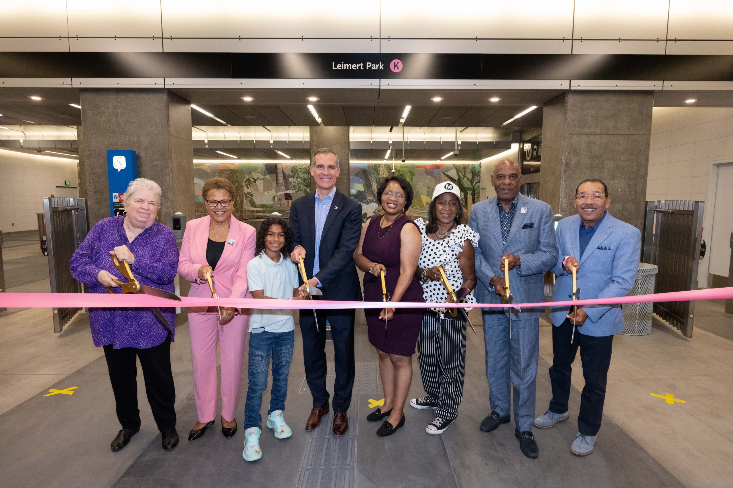 state and local officials holds scissors prior to cutting a pink ribbon in the mezzanine at leimert park station